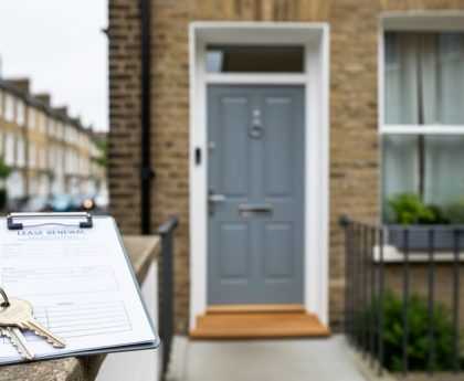 Key and clipboard beside a UK flat entrance and window, suggesting buying considerations for a short-lease apartment.